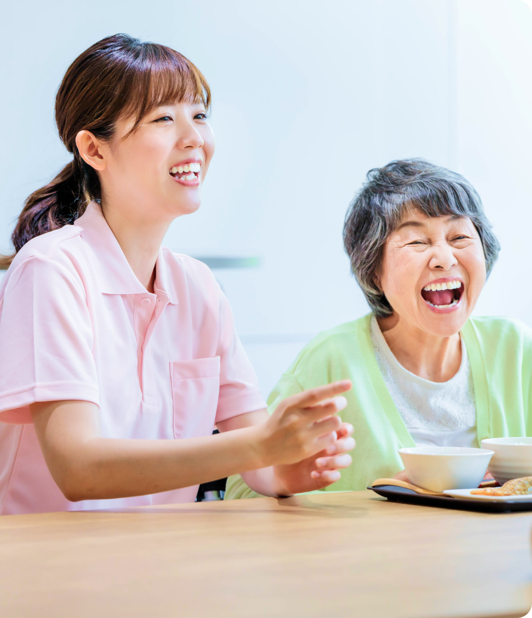 介護士と高齢女性が食卓で笑い合う様子