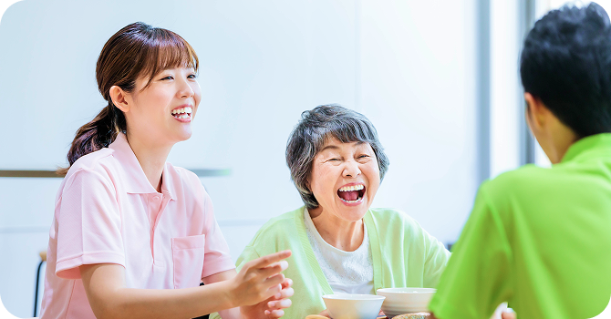 介護士と高齢女性が食卓で笑い合う様子