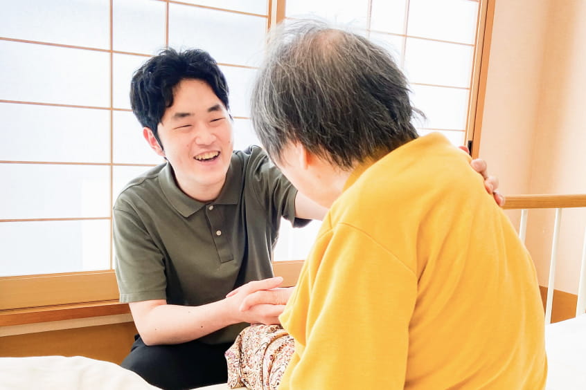 男性介護士と利用者が手を取りながら談笑