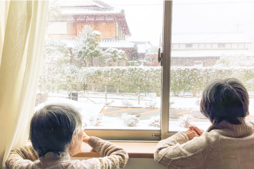 雪の降る窓の外を眺める二人