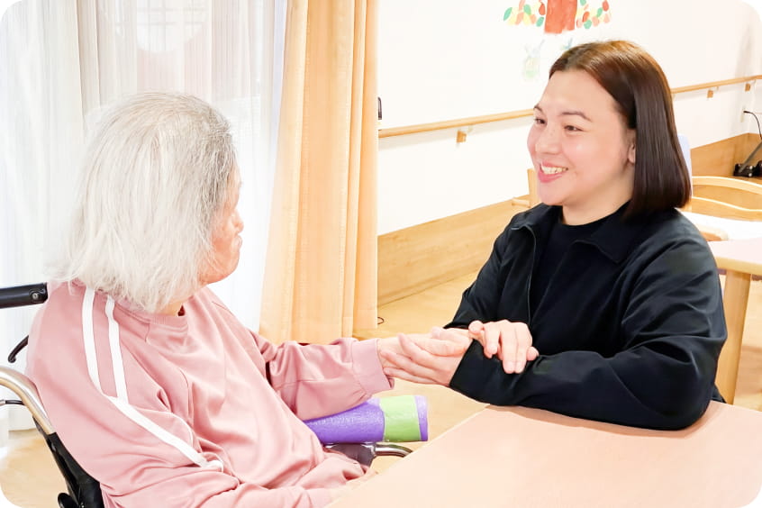 車椅子の高齢女性と手を取り合う若い女性