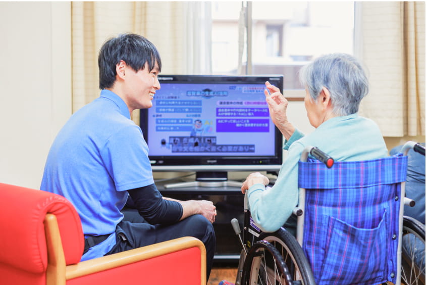 男性スタッフが高齢女性とテレビを見る
