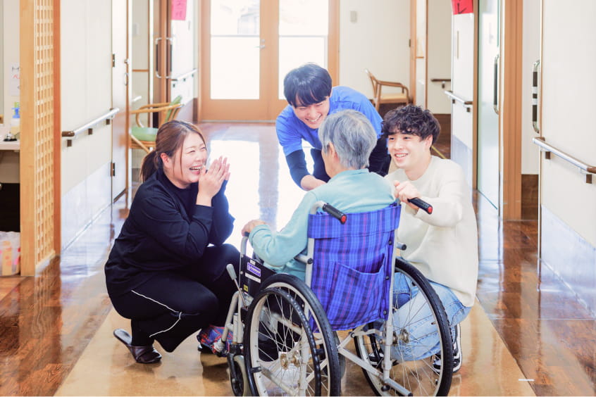 介護士と若者が車椅子の高齢女性を囲む